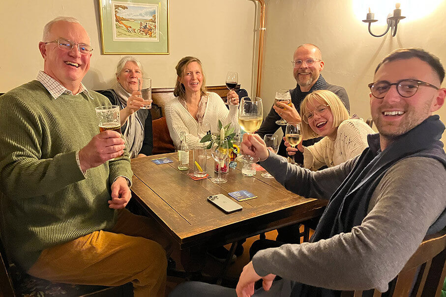 Six people enjoying beverages at the Framsden Greyhound Pub hold up raise their drinks to the camera